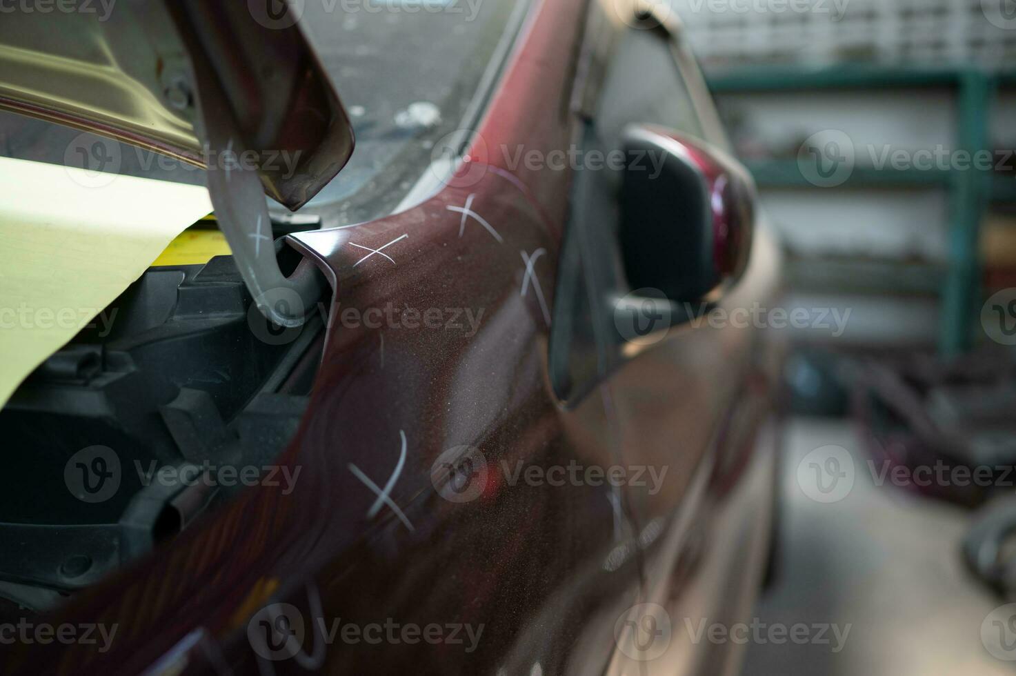 een auto monteur cheques de staat van een auto lichaam naar worden gerepareerd na een botsing. door markering de X dat nodig hebben naar worden gerepareerd foto