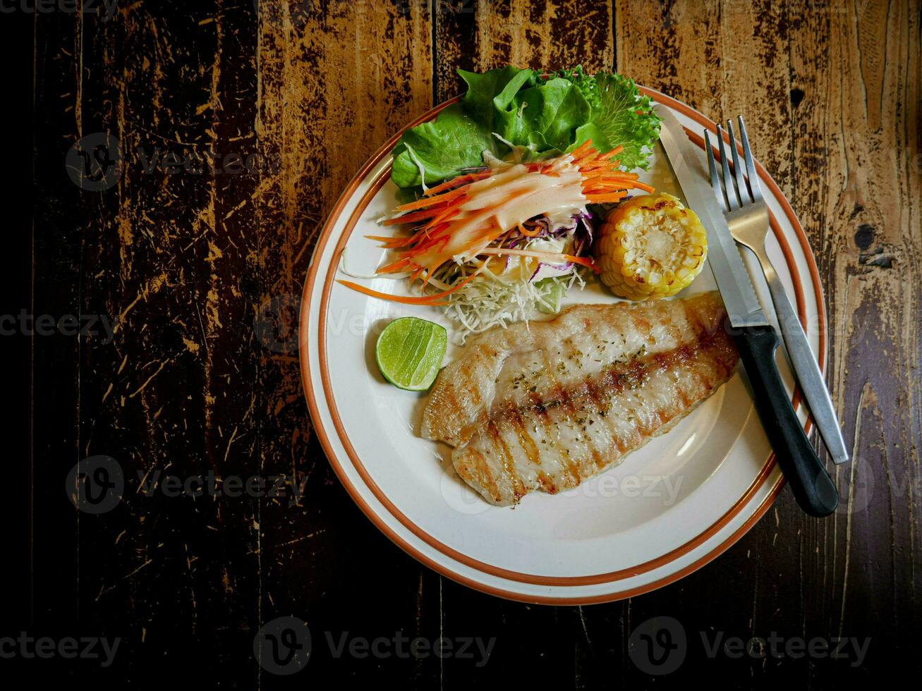 dolly vis steak bord, mes, en vork voor gemengd salade Aan een houten tafel foto