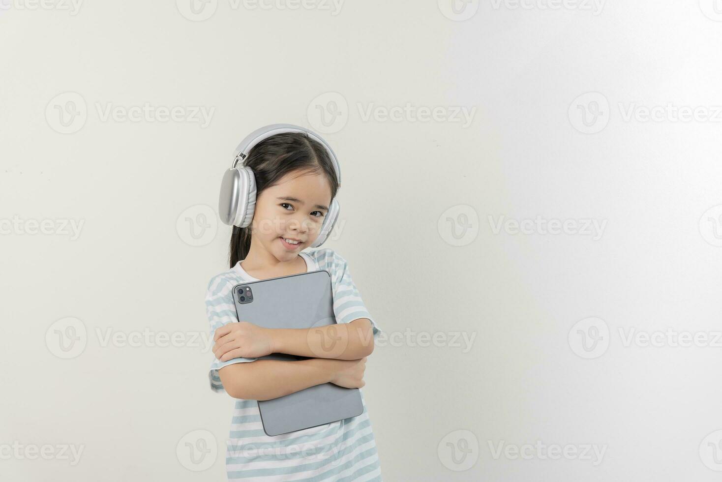 glimlachen weinig meisje stichtend en Holding een tablet met oortelefoon foto