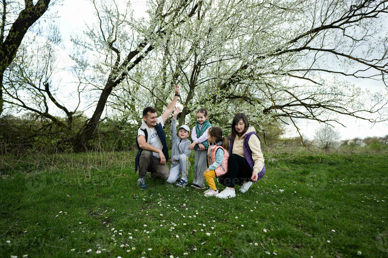 familie met drie kinderen in voorjaar weide Aan de achtergrond van een bloeiend boom. foto