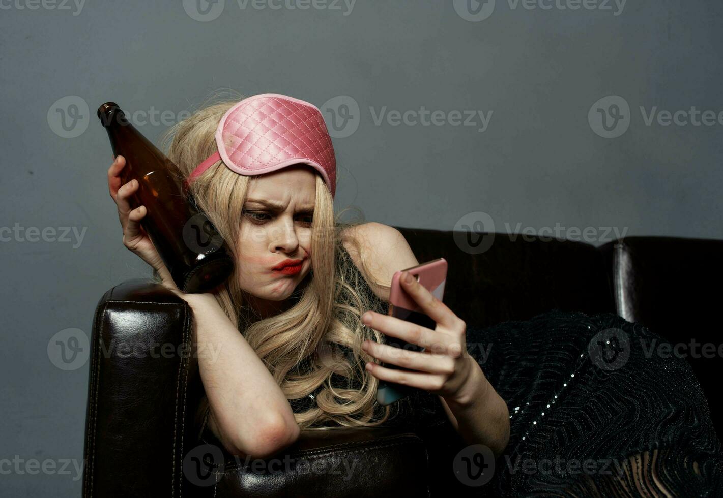 een vrouw in een roze masker leugens Aan de bankstel met een fles van bier en een telefoon in haar hand- foto
