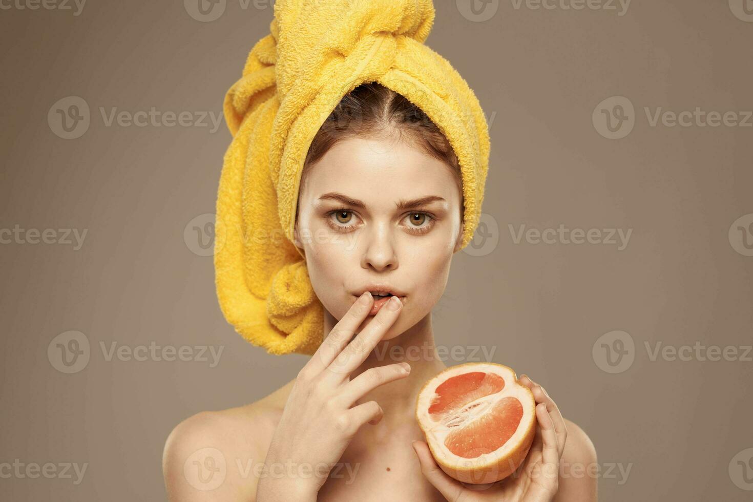 vrolijk vrouw met een geel handdoek Aan haar hoofd kaal schouders grapefruit in hand- natuurlijk schoonheidsmiddelen foto