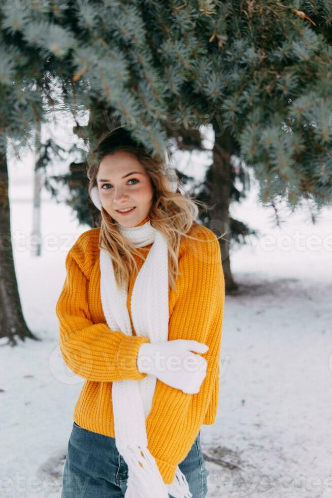 tiener blond in een geel trui buiten in winter. een tiener- meisje Aan een wandelen in winter kleren in een besneeuwd Woud foto