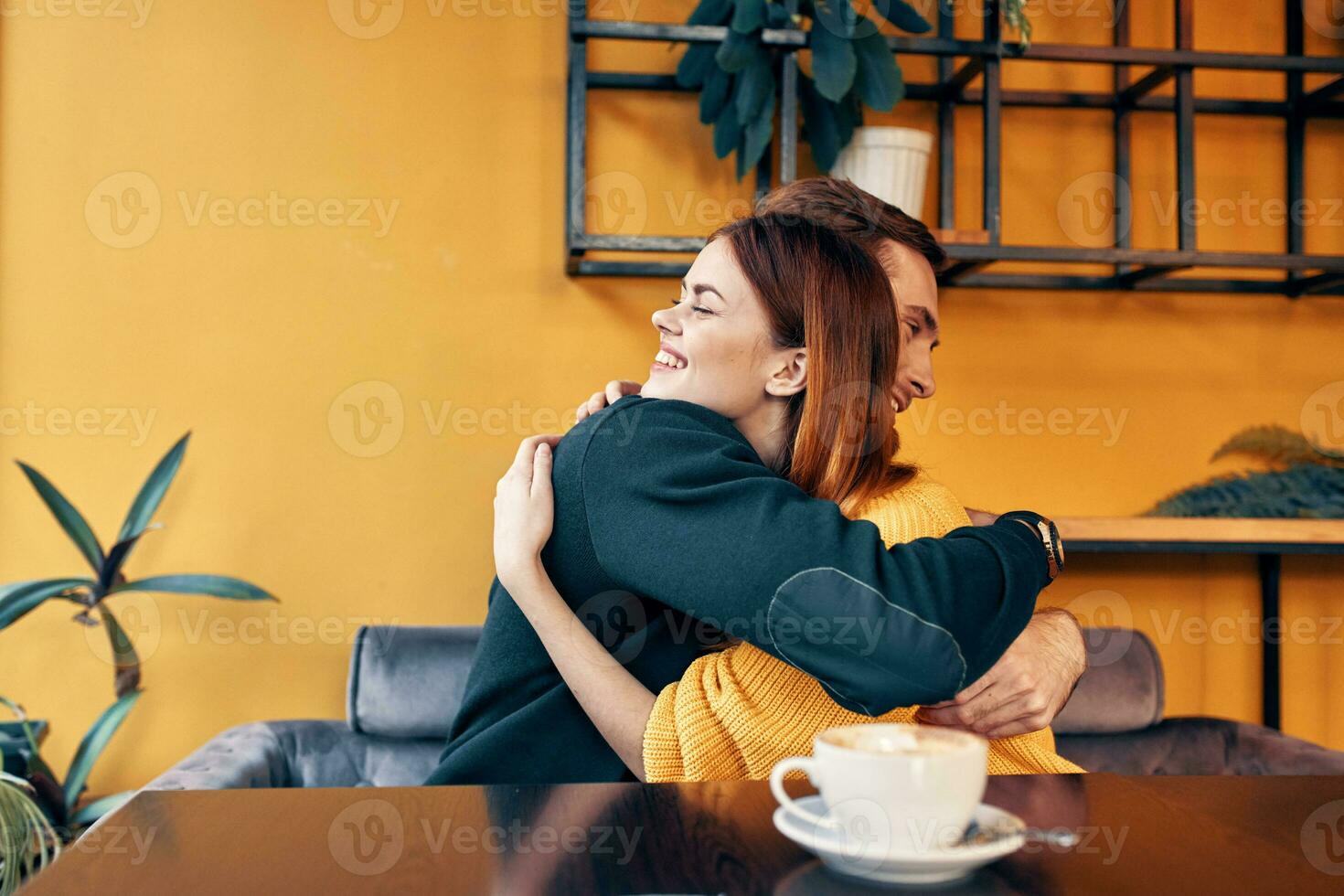 jong mensen in liefde knuffelen terwijl zittend Bij een tafel in een cafe en oranje muur interieur foto