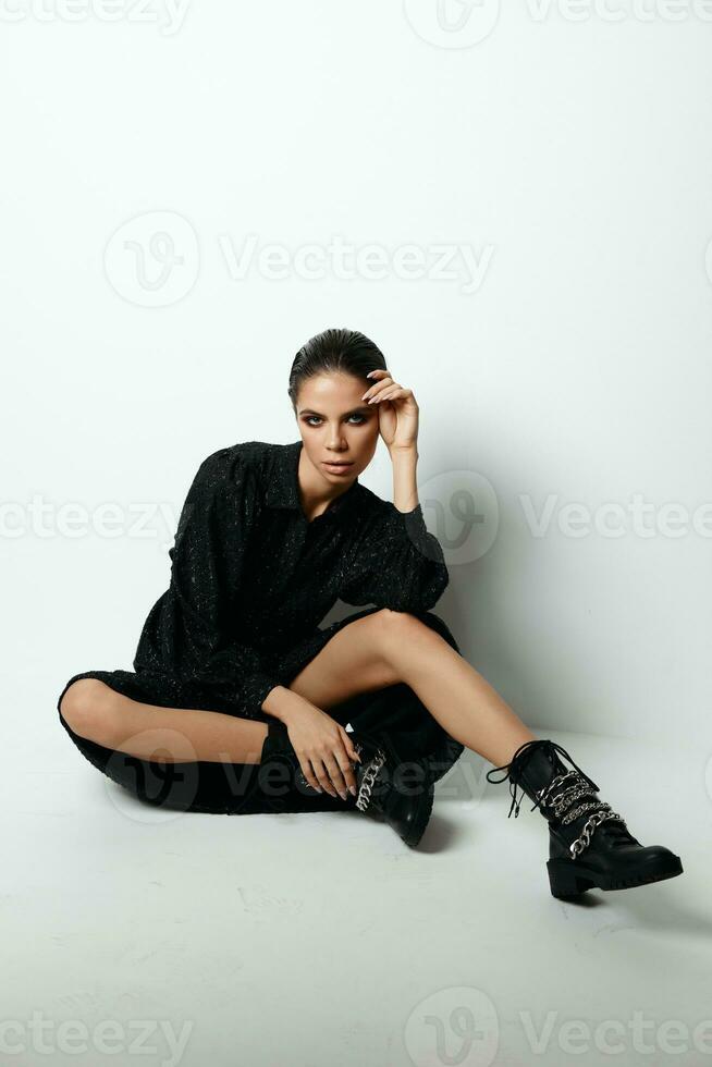 vrouw zittend Aan de verdieping in een zwart jurk mode studio laarzen foto
