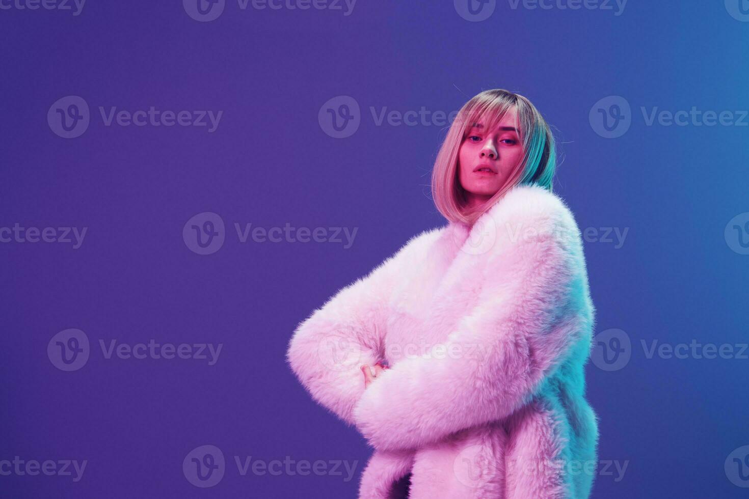 zelfverzekerd echt aanbiddelijk blond vrouw in pluizig vacht jas sparkly jurk kruis handen poseren geïsoleerd in blauw paars roze kleur licht studio achtergrond. neon partij mode concept. kopiëren ruimte banier foto