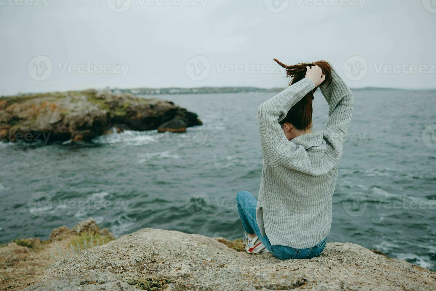vrouw zittend door de zee Holding haar haar- landschap terug visie foto