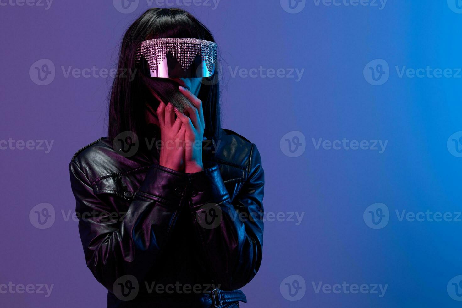 bang geschokt geweldig brunet vrouw in leer jasje modieus spiegelend zonnebril vouwen handen in de buurt gezicht poseren geïsoleerd in blauw paars kleur licht achtergrond. neon partij cyberpunk concept. kopiëren ruimte foto