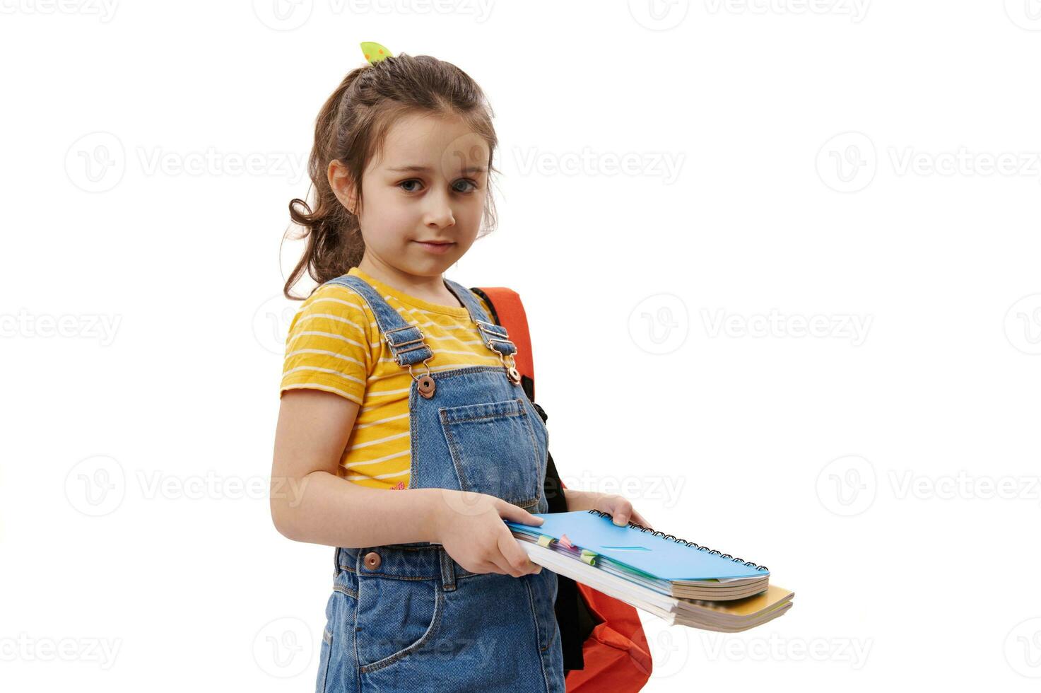 mooi kind meisje, eerste grader draag- rugzak en aan het studeren boeken, op zoek Bij camera, geïsoleerd Aan wit achtergrond foto