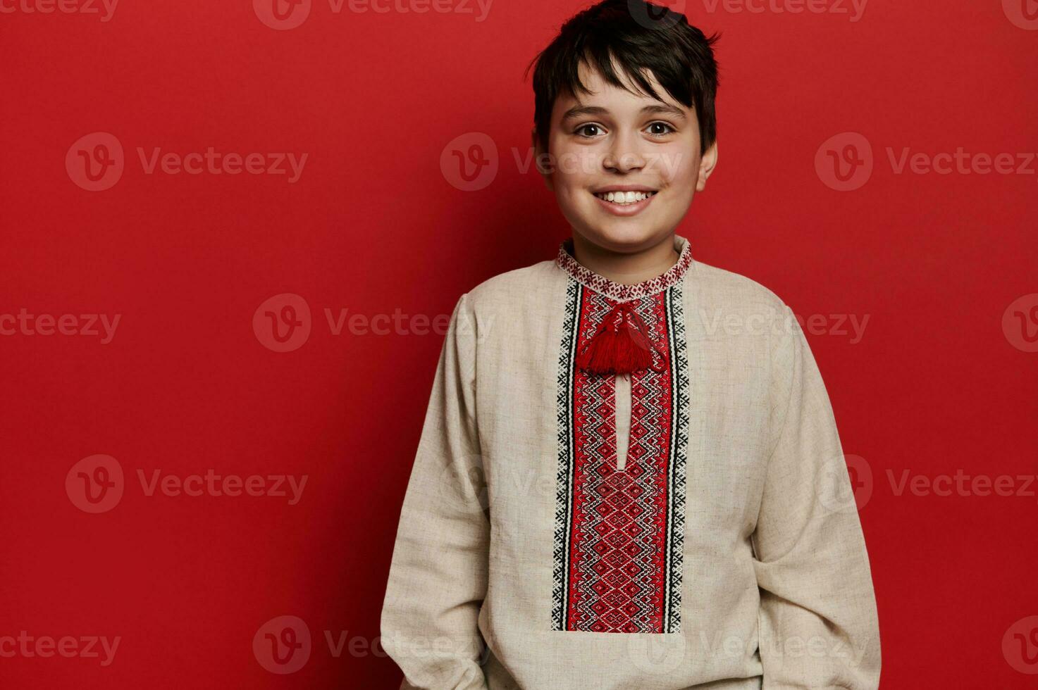 portret van een glimlachen Kaukasisch tiener jongen in oekraïens traditioneel geborduurd linnen shirt, geïsoleerd Aan rood achtergrond foto