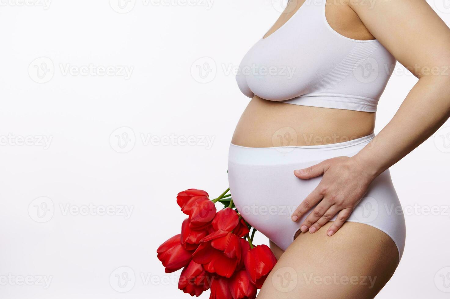 detailopname zwanger vrouw, verwachtend moeder in wit lingerie, poseren met een boeket van rood tulpen, Aan wit achtergrond foto