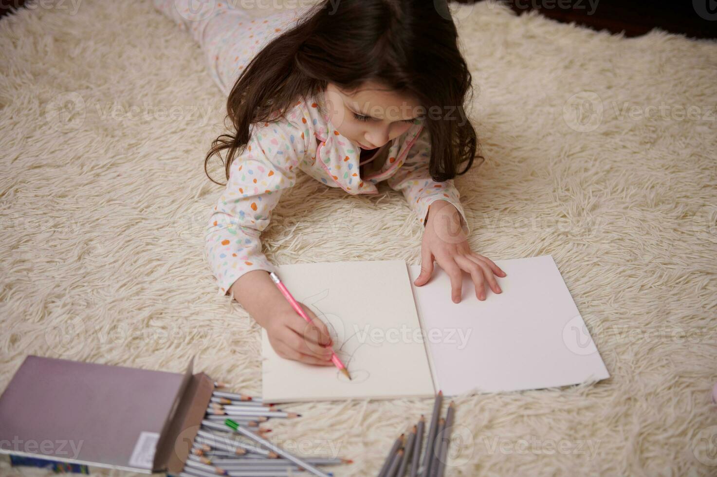 visie van bovenstaand van een Kaukasisch schattig baby meisje in elegant pyjama, tekening afbeelding met kleurrijk potloden binnenshuis foto