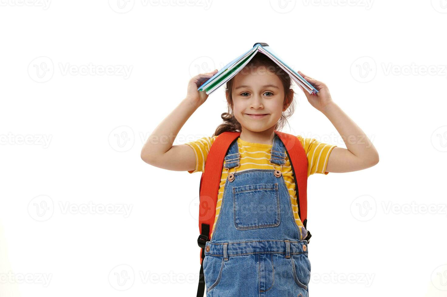 slim leerling kind meisje Holding Open boek bovenstaand haar hoofd, glimlachen op zoek Bij camera, geïsoleerd over- wit achtergrond foto