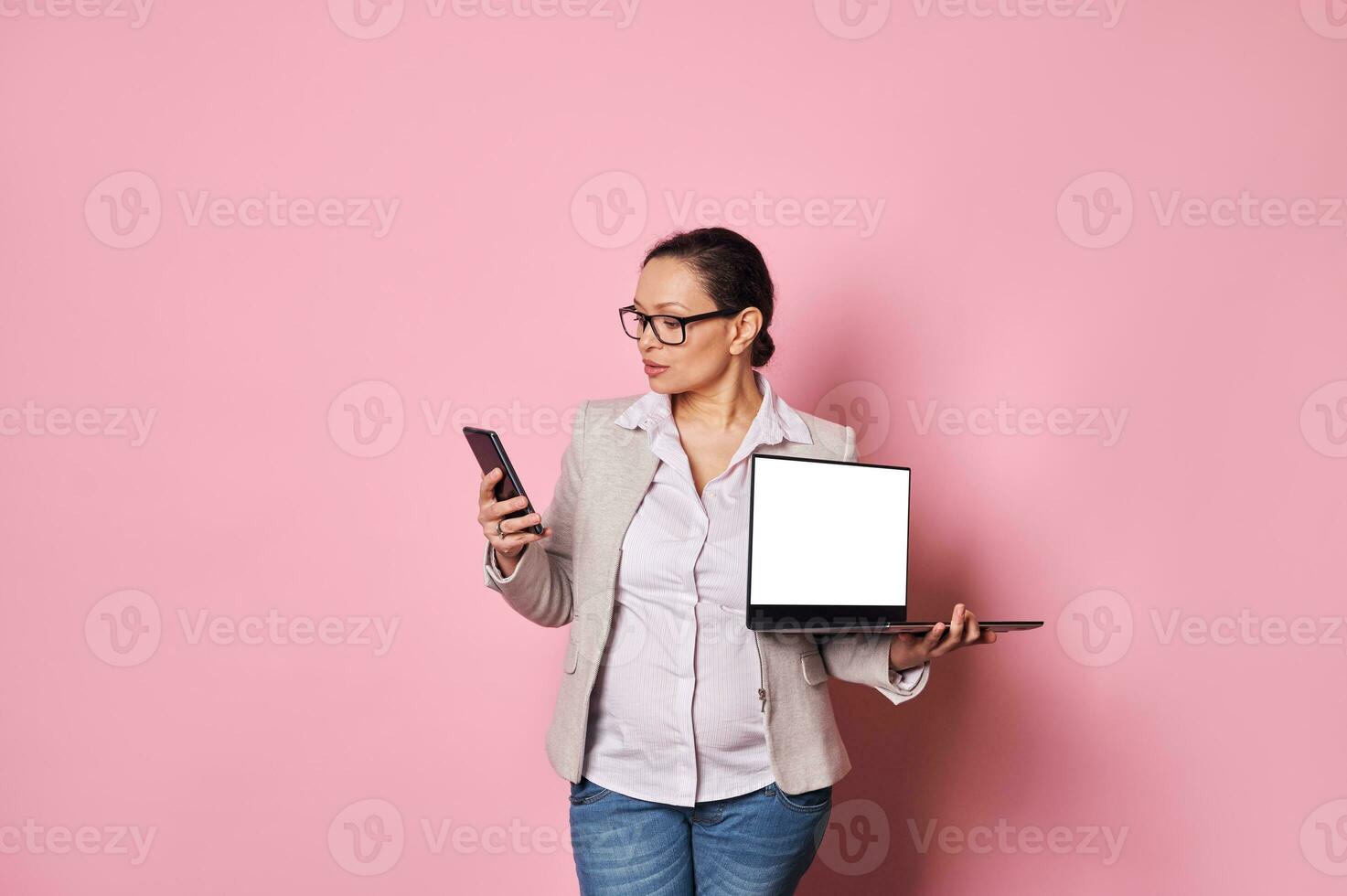 multitasking zwanger vrouw cheques smartphone, houdt laptop wit blanco scherm. mensen. zwangerschap. bedrijf. technologie foto
