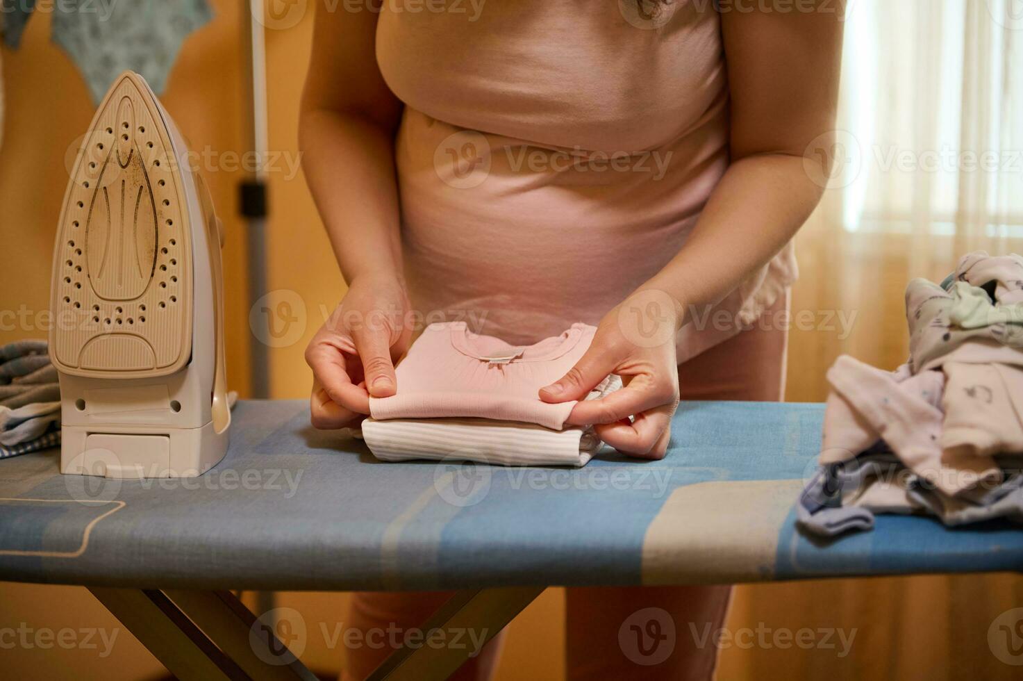 detailopname zwanger vrouw, de verwachtend moeder vouwen gestreken kleren voor pasgeborenen, bereidt zich voor zak voor de moederschap ziekenhuis foto
