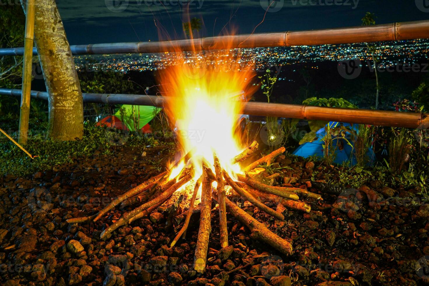 vreugdevuur en sommige vonken Aan de camping grond, met stad licht in de achtergrond foto