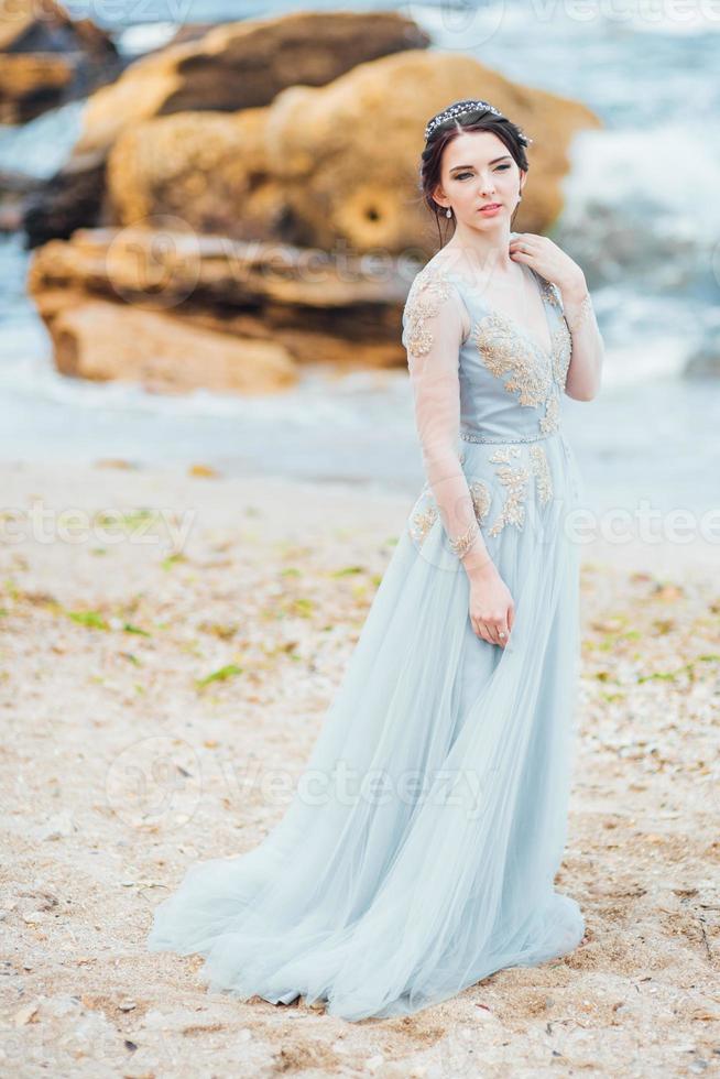 bruid in een blauwe lichte jurk die langs de oceaan loopt foto