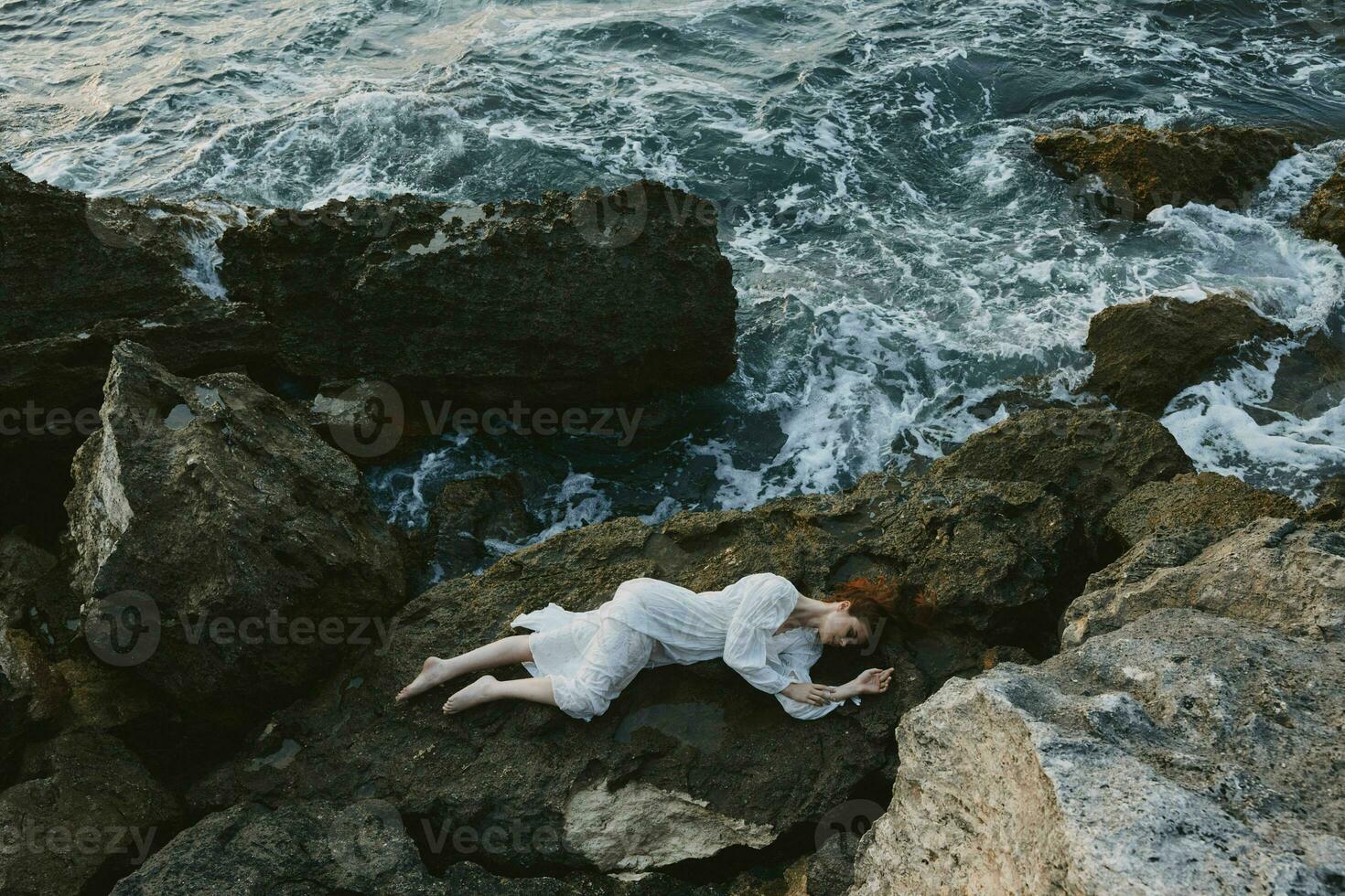 mooi vrouw in een afgelegen plek Aan een wild rotsachtig kust in een wit jurk vakantie concept foto