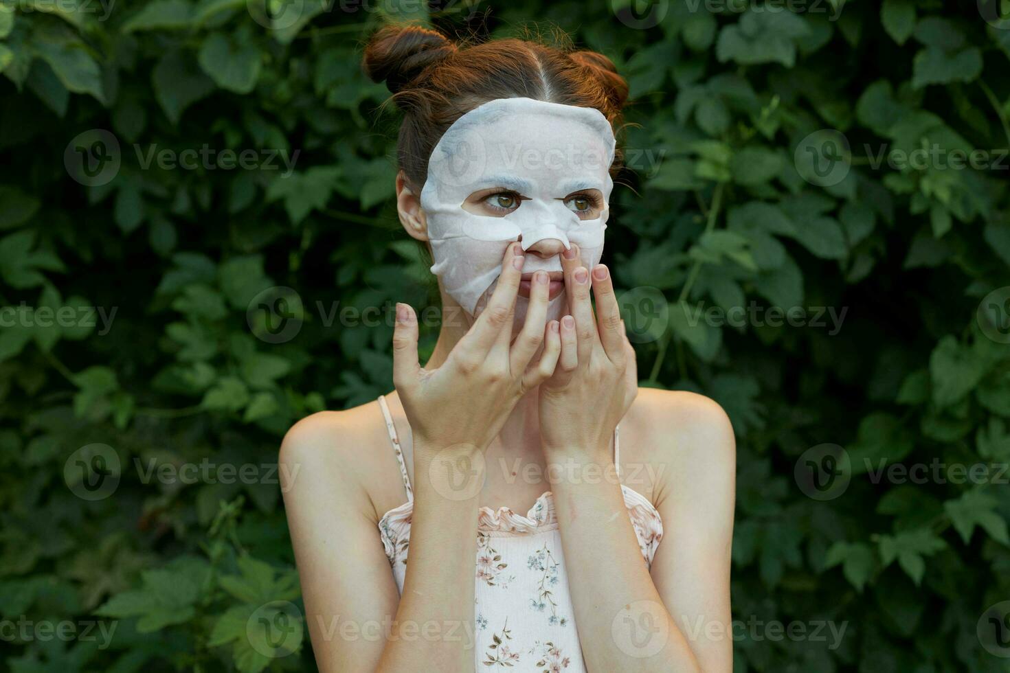 mooi hoor vrouw wit masker houdt zijn handen dichtbij naar zijn gezicht huid zorg struiken in de achtergrond foto