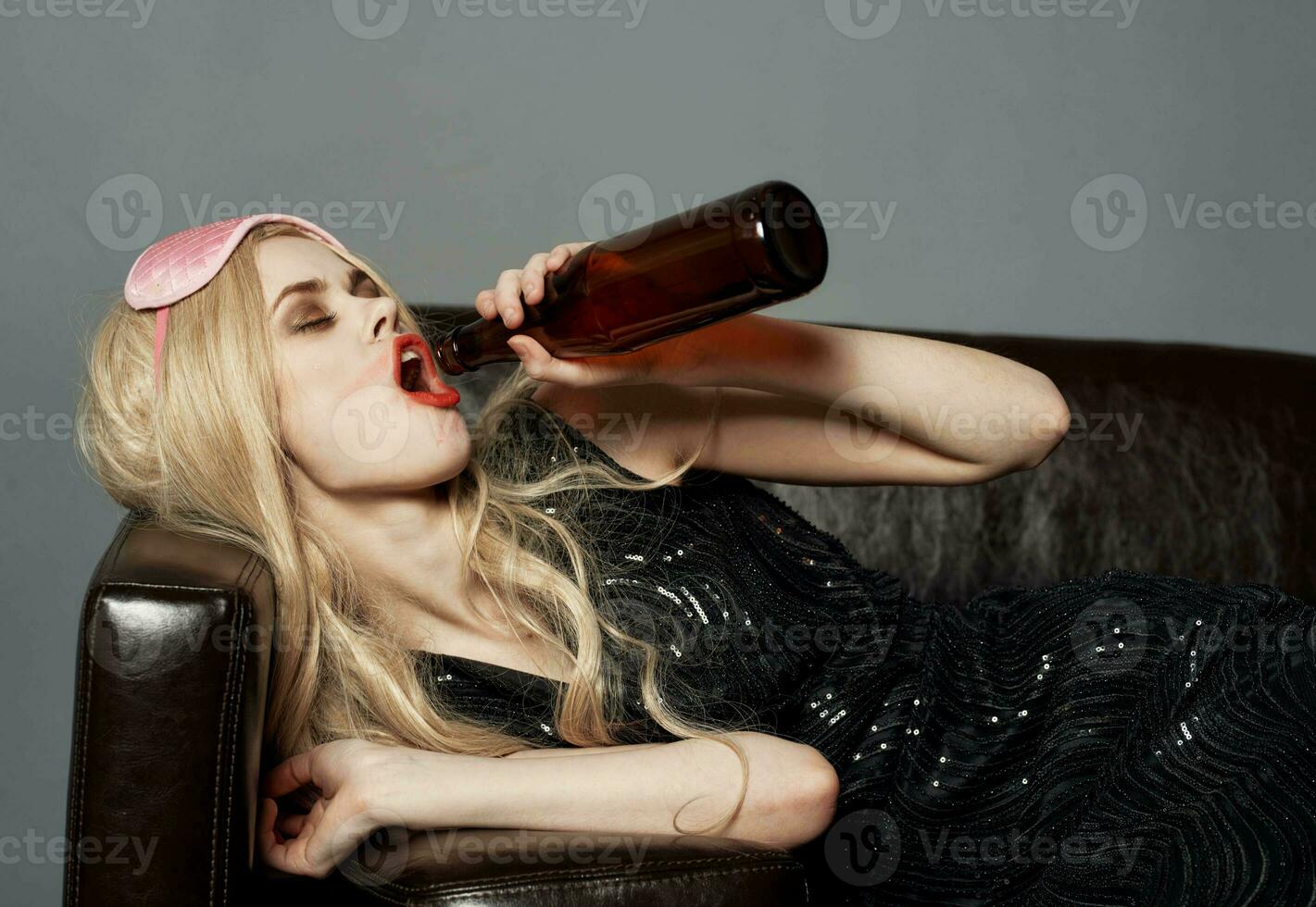 een vrouw met een roze masker Aan haar hoofd en een fles van bier slaapt Aan de bankstel foto
