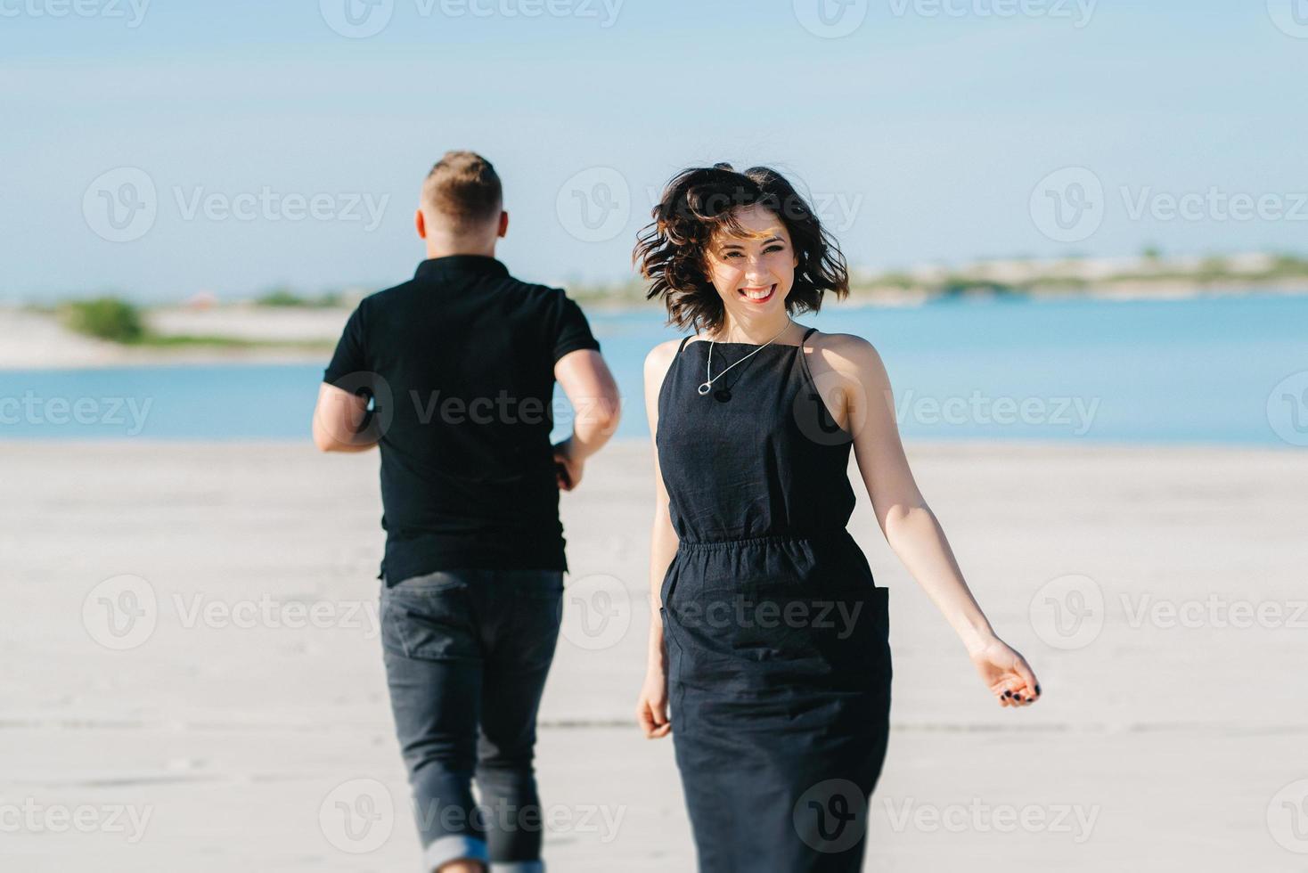 jong stel een man met een meisje in zwarte kleren lopen op het witte zand foto