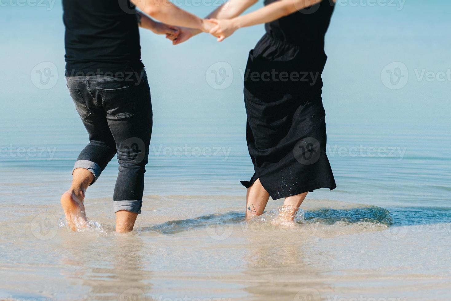 jong stel een man met een meisje in zwarte kleren lopen op het witte zand foto