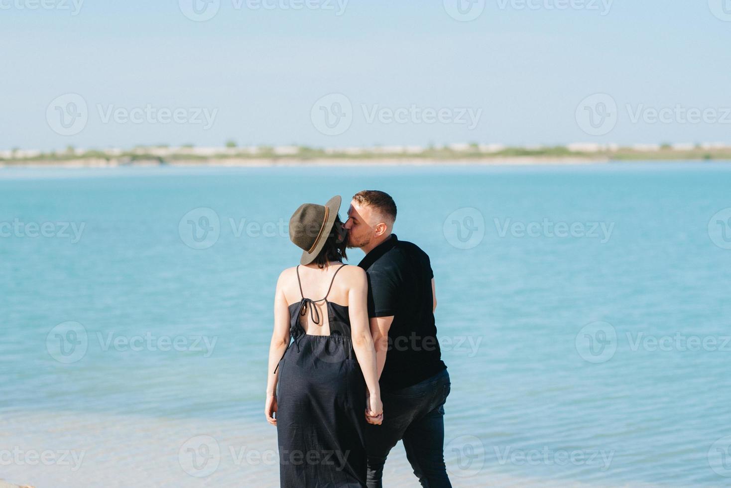 jong stel een man met een meisje in zwarte kleren lopen op het witte zand foto