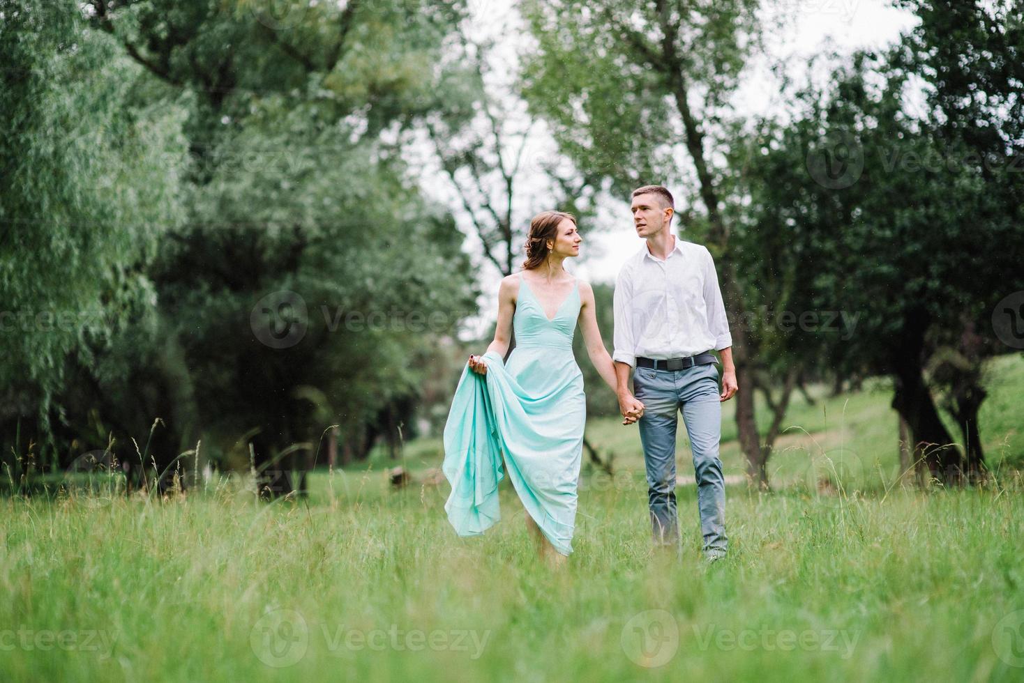 gelukkige man in een wit overhemd en een meisje in een turquoise jurk lopen in het bospark foto