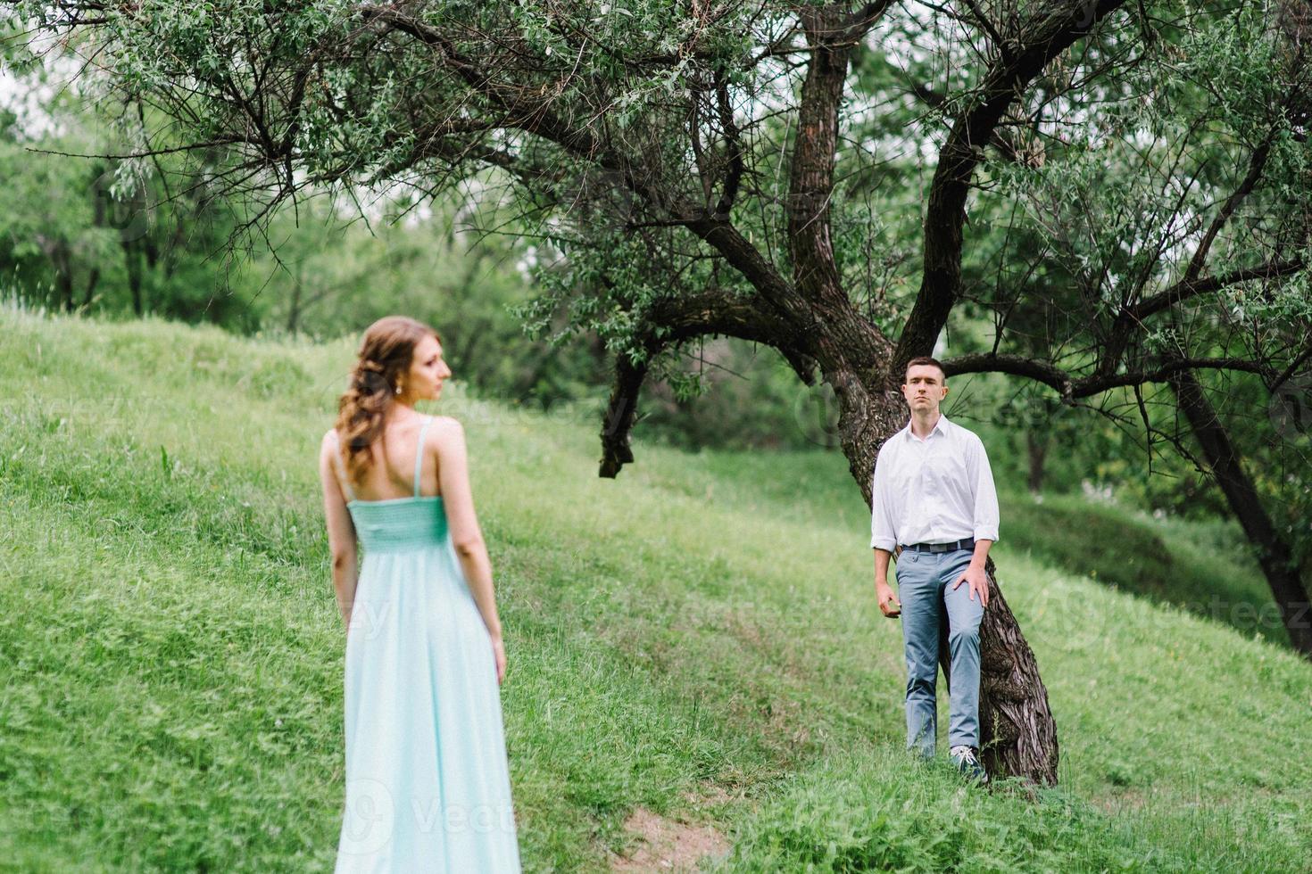 gelukkige man in een wit overhemd en een meisje in een turquoise jurk lopen in het bospark foto