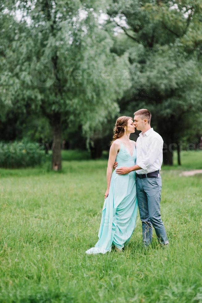 gelukkige man in een wit overhemd en een meisje in een turquoise jurk lopen in het bospark foto
