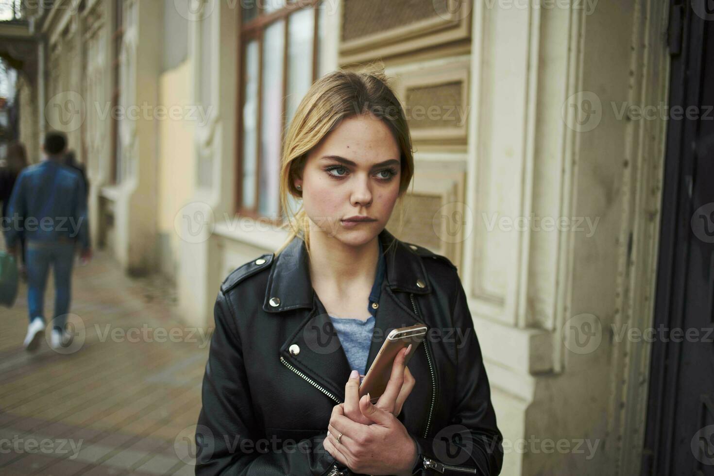 vrouw Aan de straat met een telefoon in haar handen leer jasje wandelen in de buurt de gebouw foto