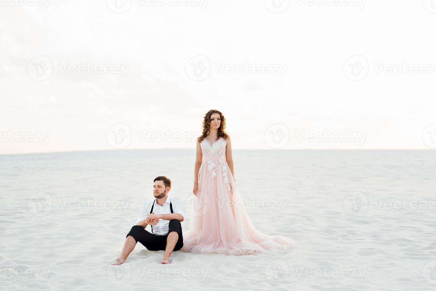 jong stel een man in zwarte rijbroek en een meisje in een roze jurk lopen langs het witte zand foto