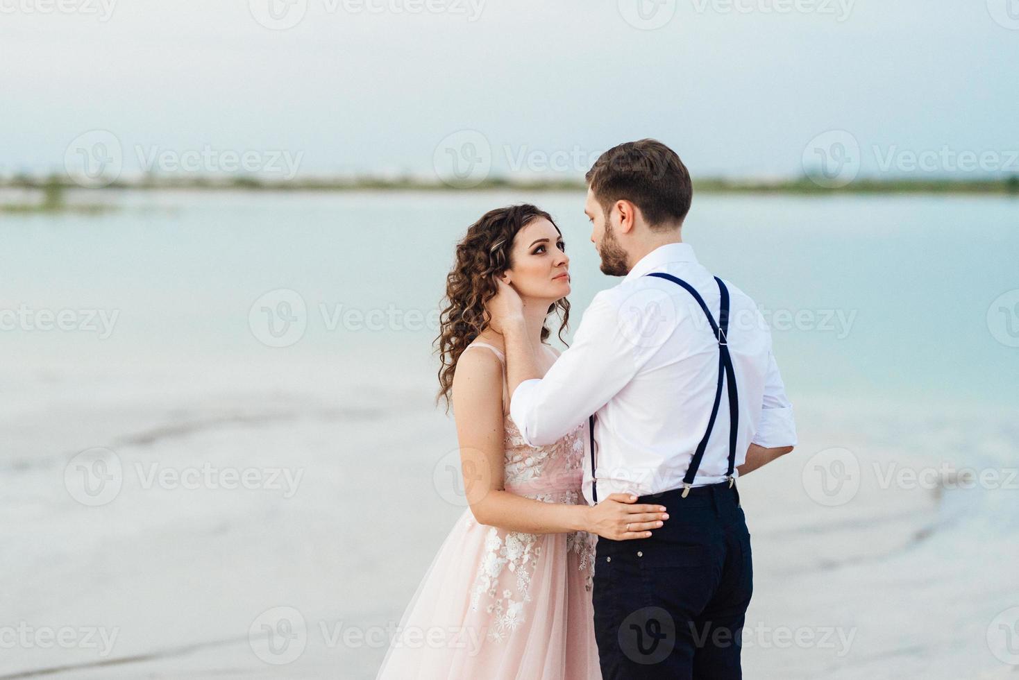 jong stel een man in zwarte rijbroek en een meisje in een roze jurk lopen langs het witte zand foto