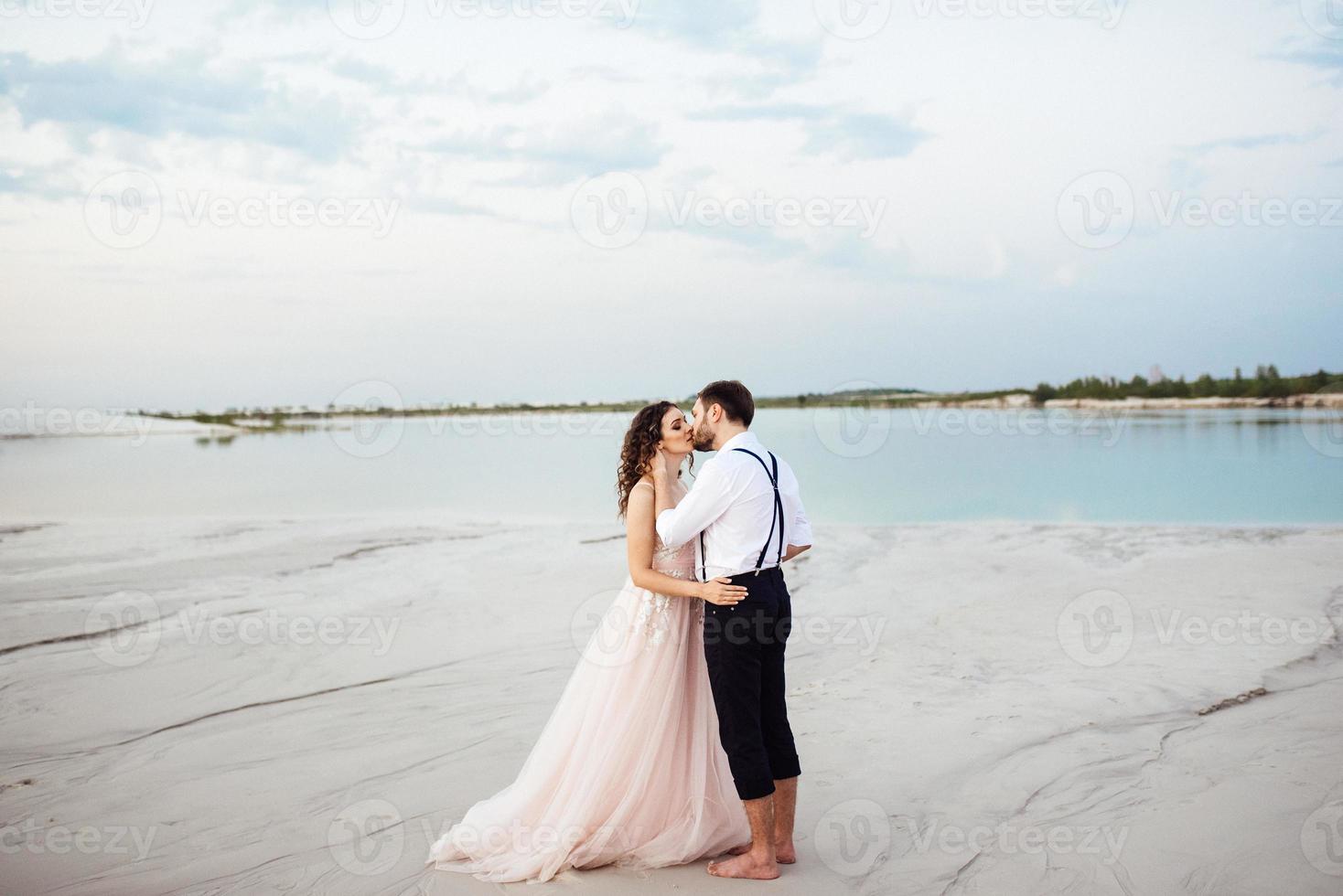 jong stel een man in zwarte rijbroek en een meisje in een roze jurk lopen langs het witte zand foto