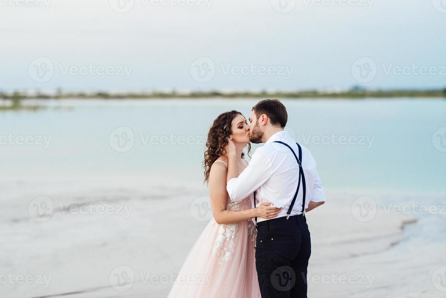 jong stel een man in zwarte rijbroek en een meisje in een roze jurk lopen langs het witte zand foto