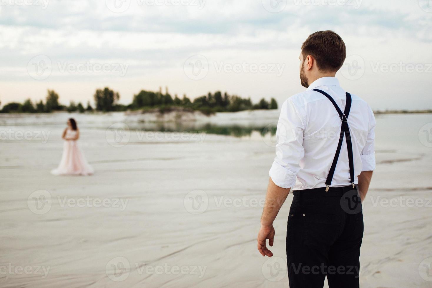 jong stel een man in zwarte rijbroek en een meisje in een roze jurk lopen langs het witte zand foto