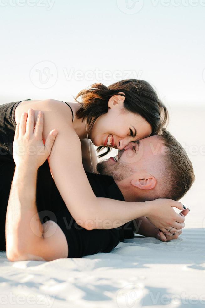 jong koppel een jongen en een meisje met vrolijke emoties in zwarte kleding lopen door de witte woestijn foto