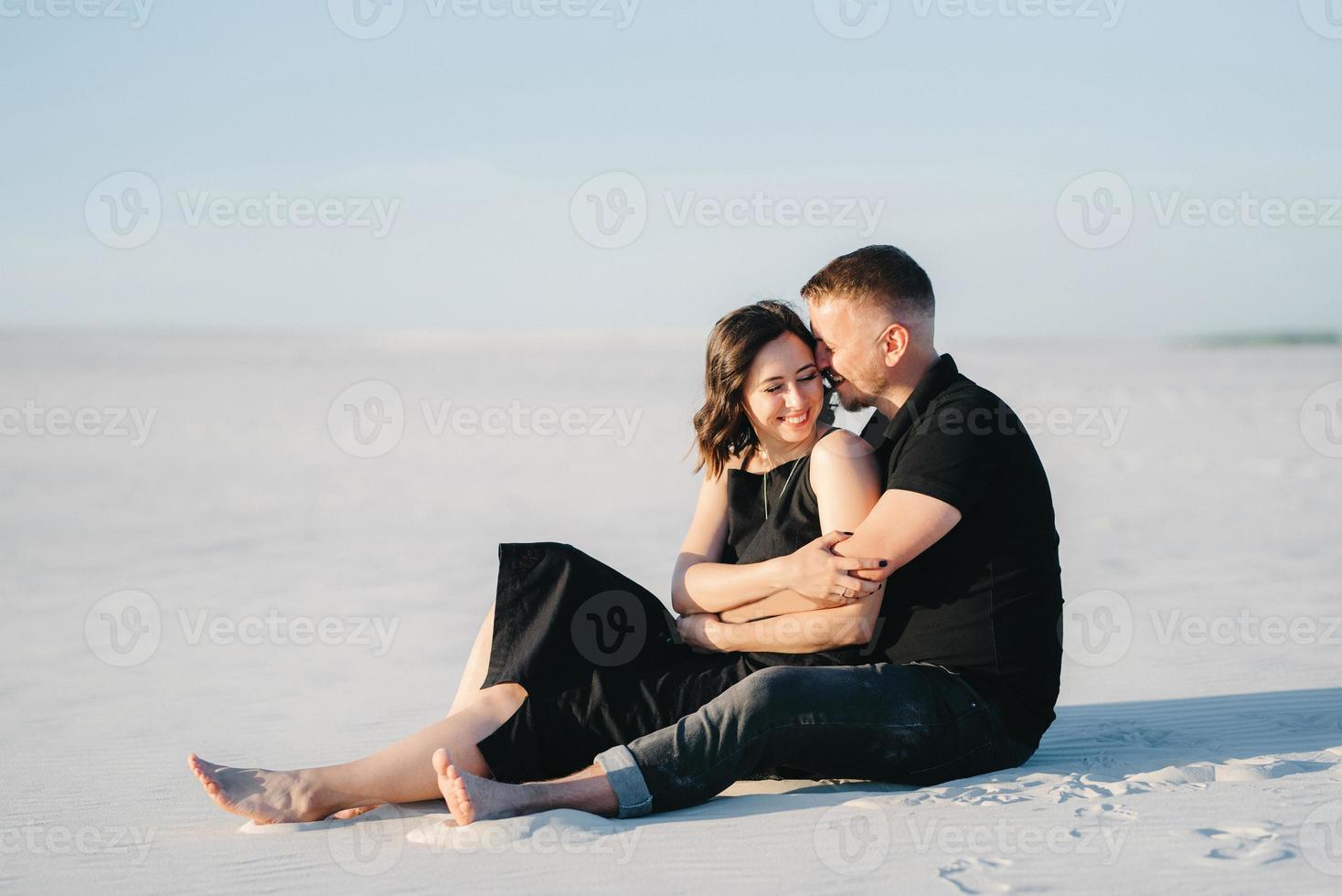 jong koppel een jongen en een meisje met vrolijke emoties in zwarte kleding lopen door de witte woestijn foto