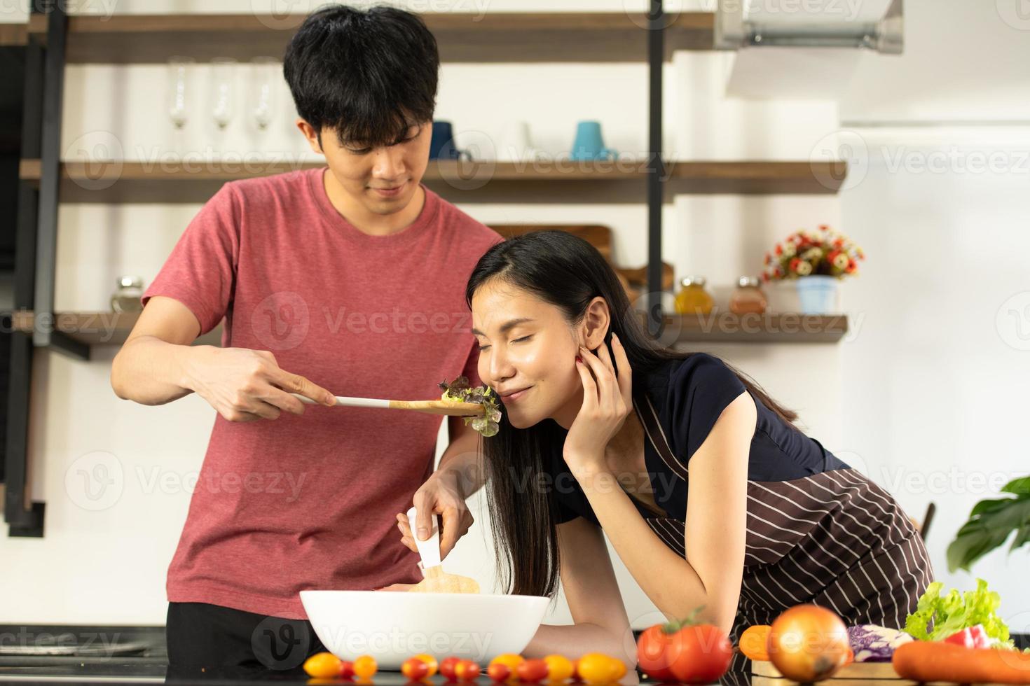 een jong Aziatisch stel eet samen en lacht vrolijk terwijl ze hun salade in de keuken koken. foto
