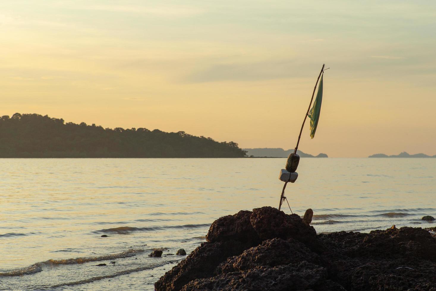 selectieve focus op een gescheurde vlag op een oude bamboestok in de rots aan de kust foto