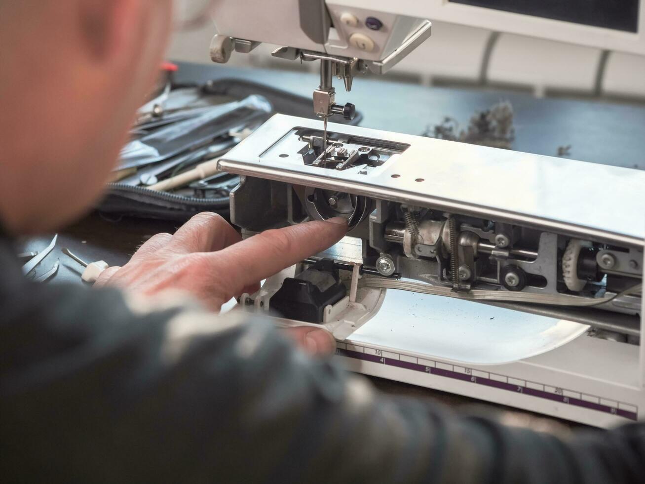 mannetje meester reparaties de naaien machine. professioneel aanpassing van een naaien machine in een klein fabriek. schoonmaak en reparatie van professioneel apparatuur. foto