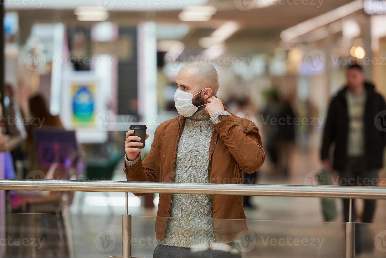 een man zet een masker op terwijl hij een kopje koffie vasthoudt in het winkelcentrum foto