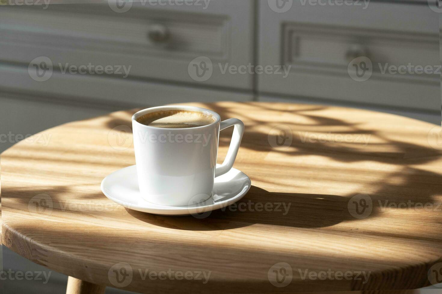 een wit porselein kop met koffie Aan een schotel staat Aan een ronde tafel foto