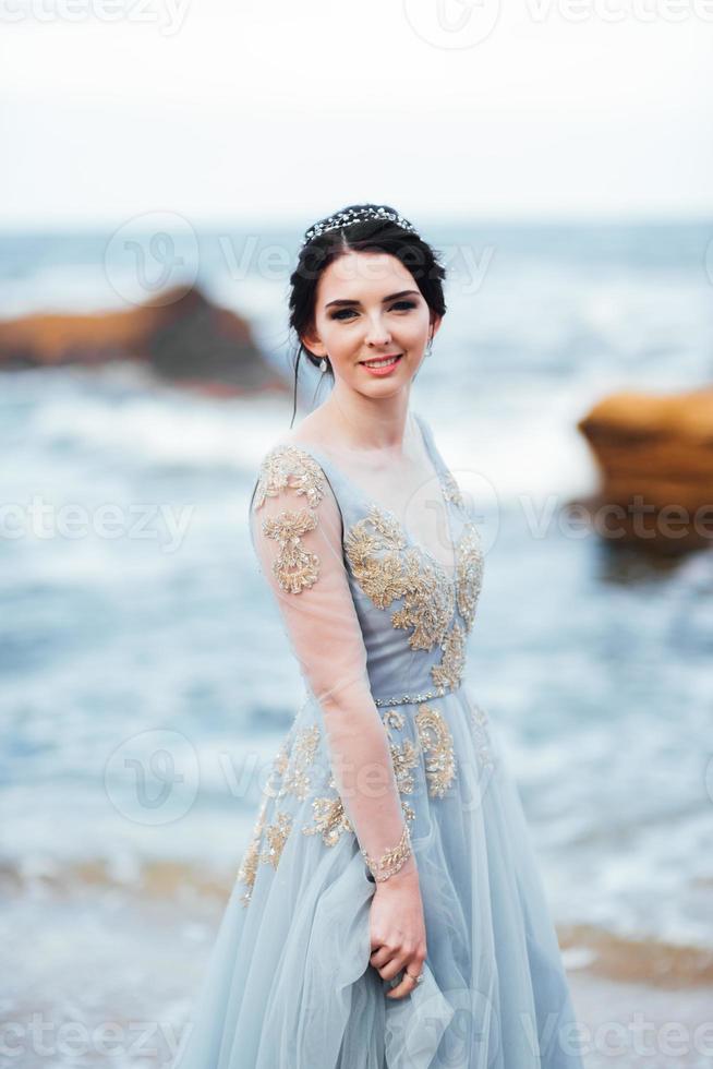 bruid in een blauwe lichte jurk die langs de oceaan loopt foto