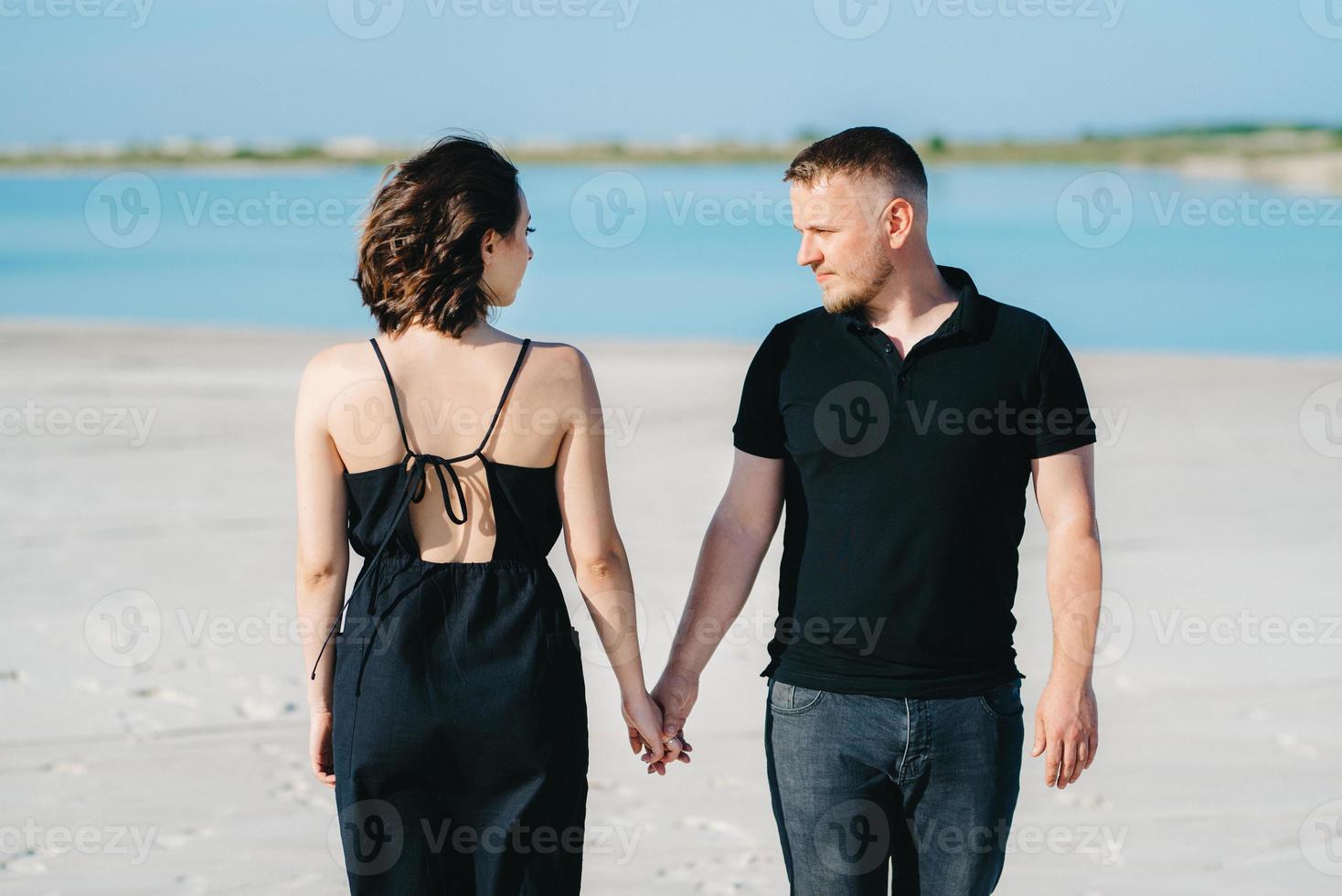jong stel een man met een meisje in zwarte kleren lopen op het witte zand foto