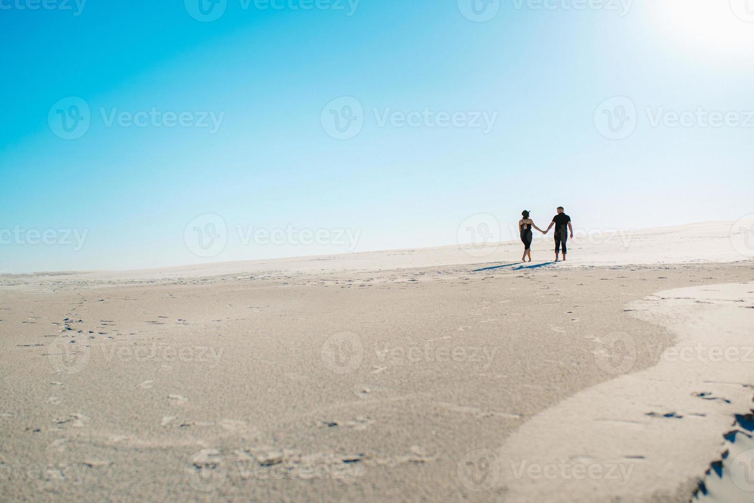 jong koppel een jongen en een meisje met vrolijke emoties in zwarte kleding lopen door de witte woestijn foto