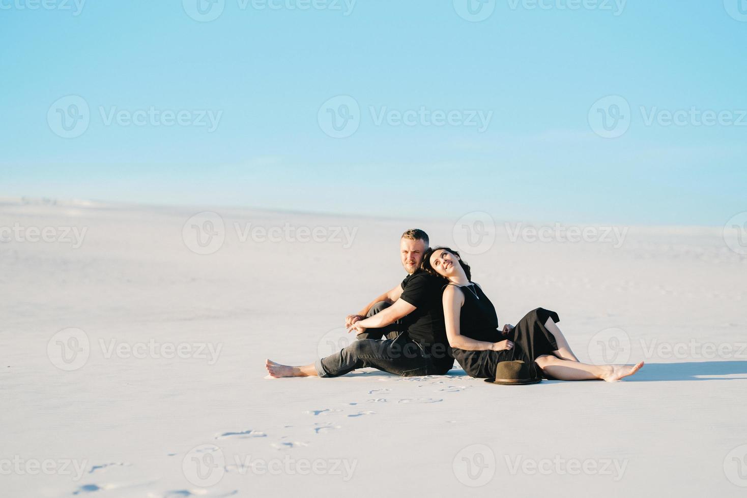 jong koppel een jongen en een meisje met vrolijke emoties in zwarte kleding lopen door de witte woestijn foto