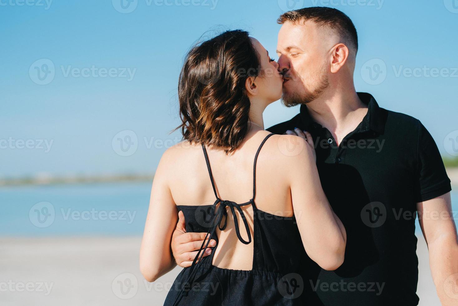 jong stel een man met een meisje in zwarte kleren lopen op het witte zand foto