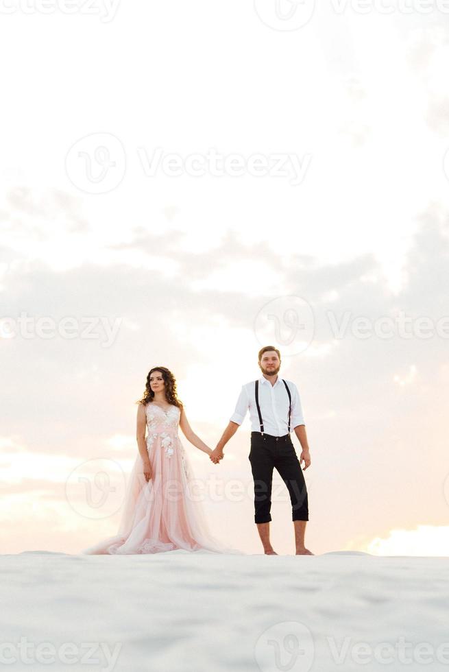 jong stel een man in zwarte rijbroek en een meisje in een roze jurk lopen langs het witte zand foto