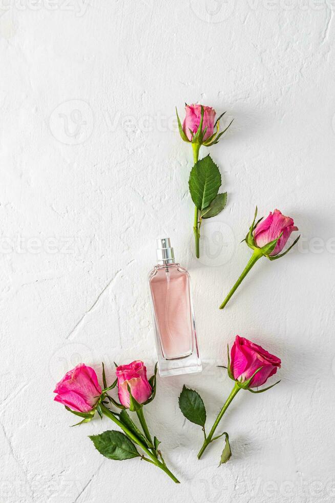 een elegant fles van vrouwen parfum Aan een wit getextureerde achtergrond tussen leven roze rozenknopjes. top verticaal visie. vlak leggen. een sjabloon voor een Product. foto